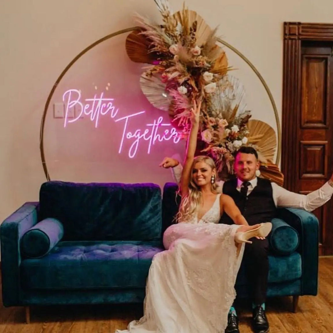 Better Together LED Neon Light Sign in pink, featuring script lettering on a floral wedding backdrop behind a seated couple.