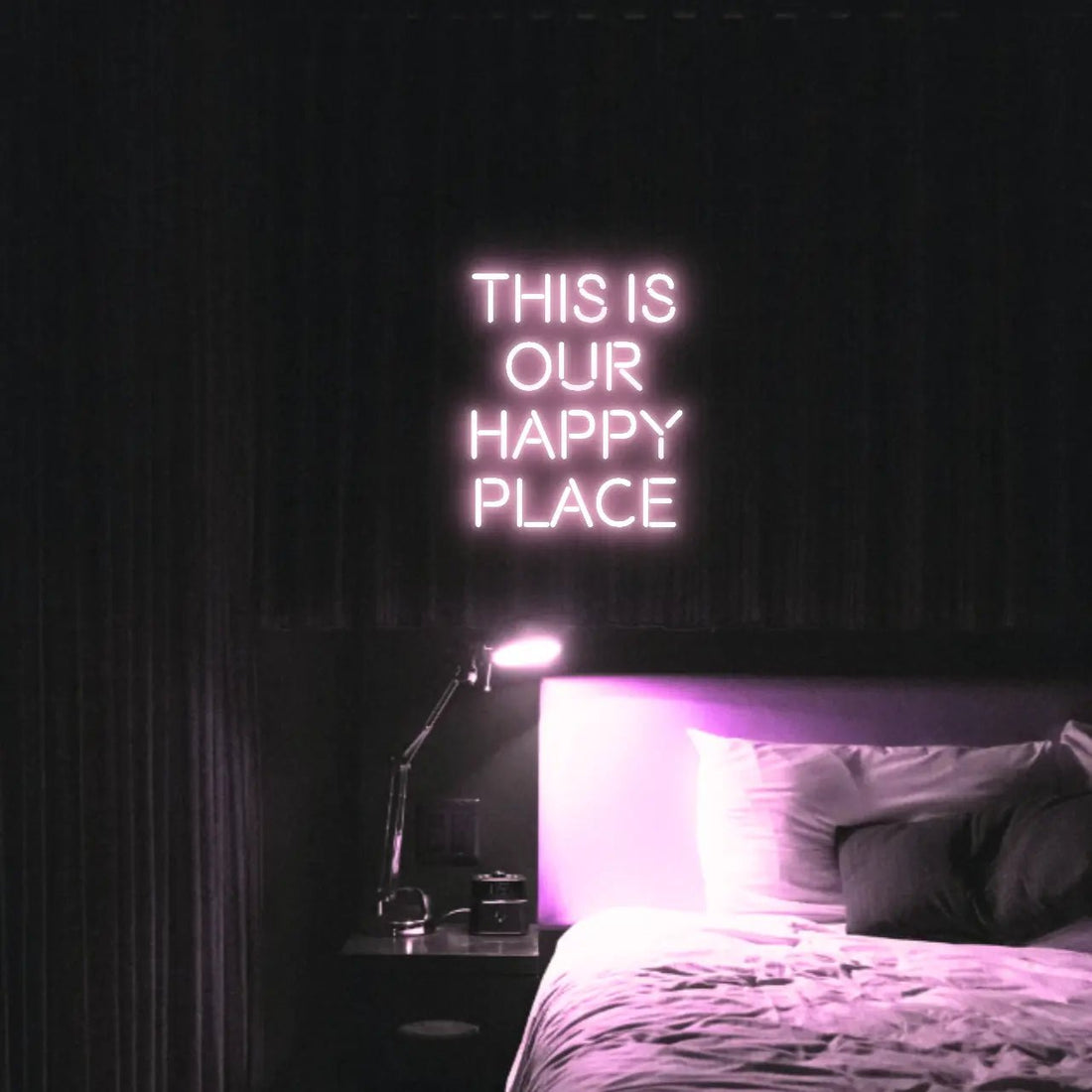 This is our happy place LED Neon Light Sign in pale pink, featuring stacked block lettering illuminated above a bed.