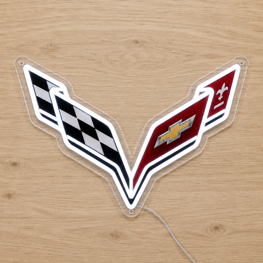 A clear acrylic LED light shaped like the Chevrolet Corvette C-word emblem, featuring a black-and-white checkered flag on one side, the Chevrolet bowtie on a red side, and a white side with a small emblem, displayed on a light wood background.