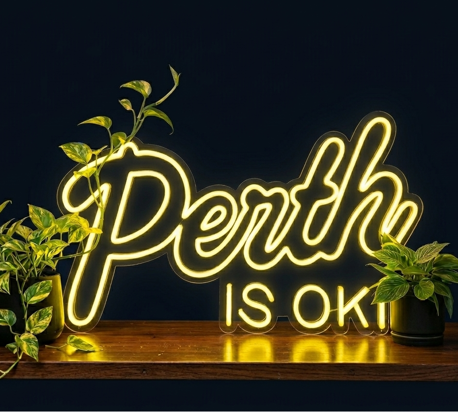 Neon sign with 'Perth is OK!' text on a dark background with plants.