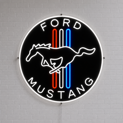 A circular Ford Mustang neon-style wall sign mounted on a white brick wall. The sign has a black background with a white running horse logo, white 'FORD' at the top and 'MUSTANG' at the bottom, and three vertical stripes in red, white, and blue.
