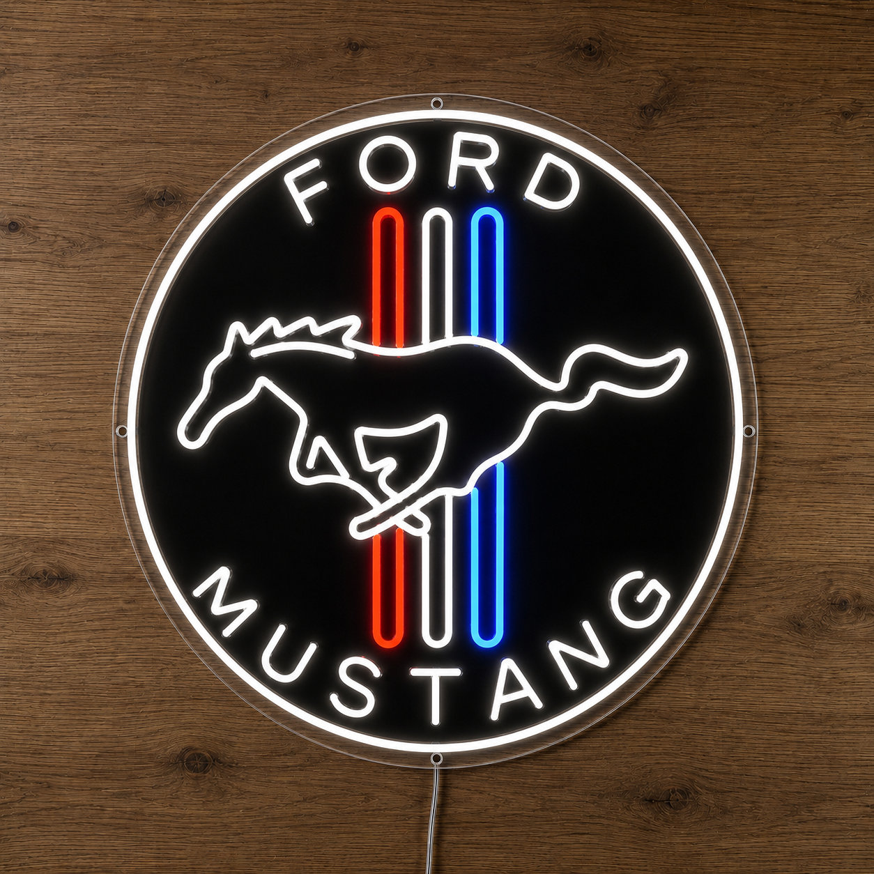 A circular Ford Mustang neon-style wall sign mounted on a wooden surface. The sign has a black background with a glowing white outline and the words “FORD” at the top and “MUSTANG” at the bottom, plus the classic horse emblem in white over vertical red, white, and blue stripes.