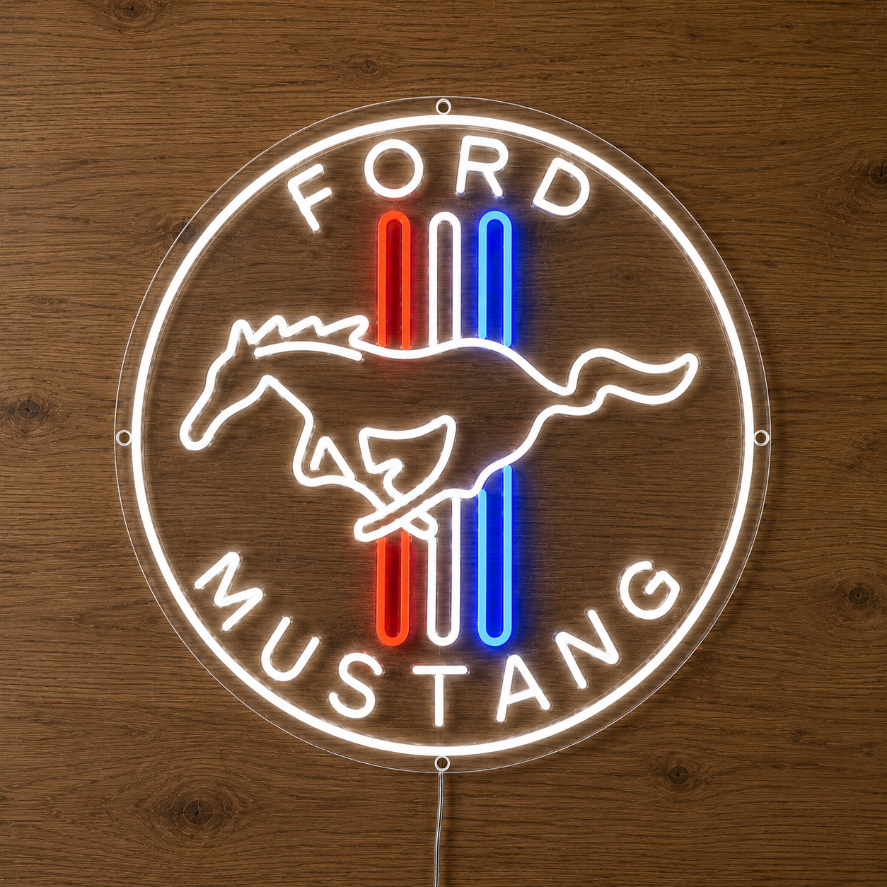 A circular LED neon-style Ford Mustang sign mounted against a wooden wall. The sign features a white glowing outline with the words 'FORD' at the top and 'MUSTANG' at the bottom, a white running horse silhouette, and three vertical stripes in red and blue in the center.