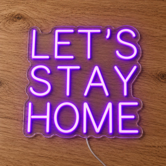 Let's Stay Home LED Neon Sign in purple, featuring three lines of block lettering on a wooden surface.