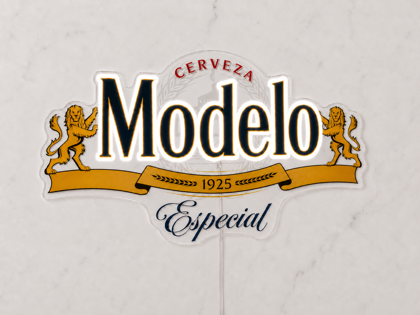 A die-cut decorative sign featuring the Cerveza Modelo Especial logo, with two gold lions, black and red lettering, and a gold ribbon banner, displayed against a light marble background.