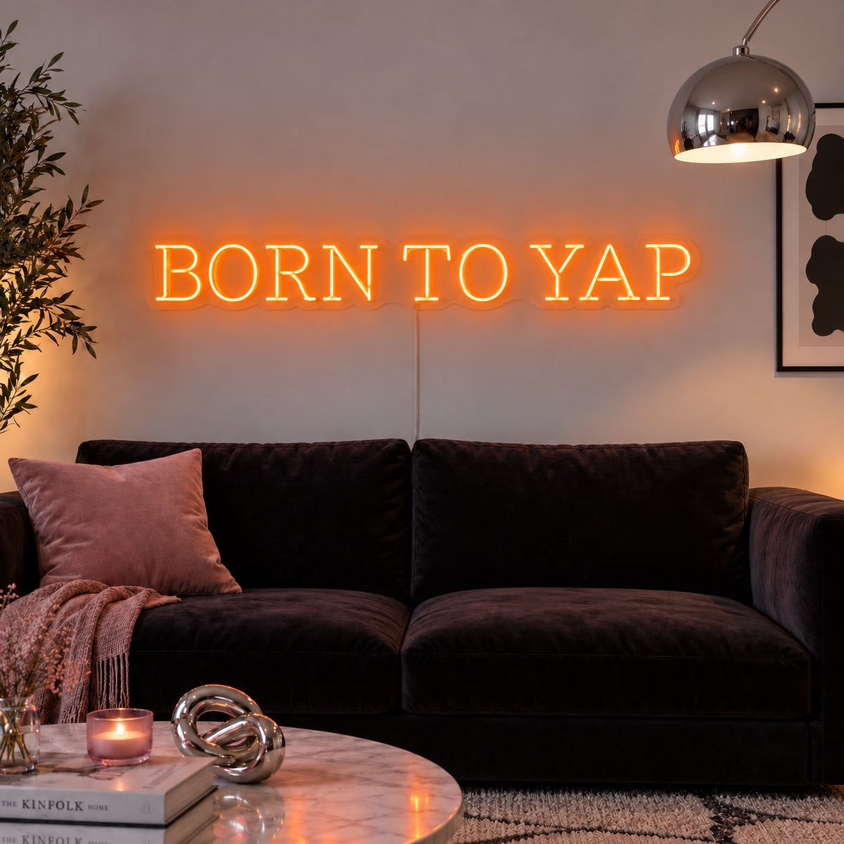 Orange version of the Born To Yap Neon Sign, shown above a dark sofa and glass coffee table.
