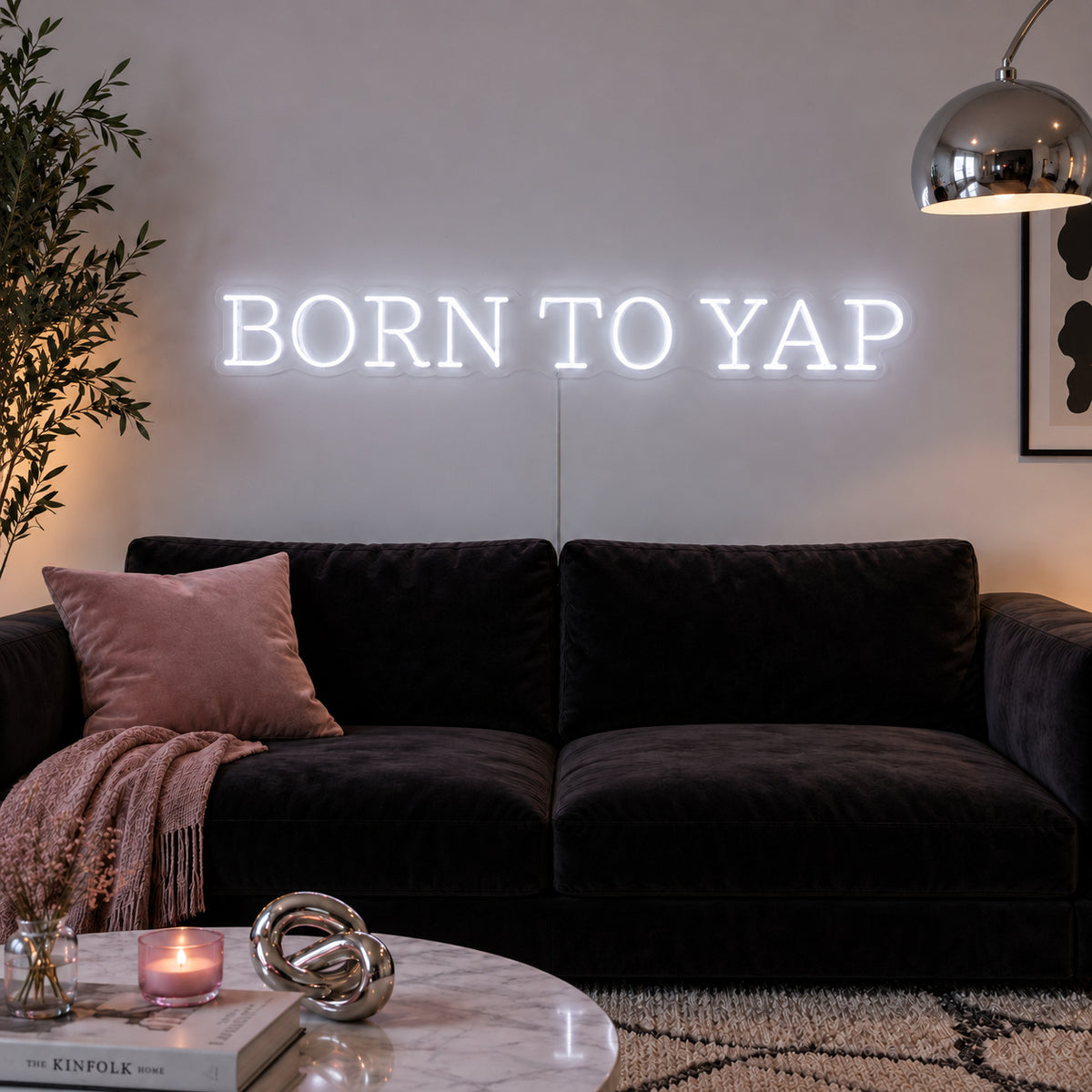 Born To Yap Neon Sign glowing white above a dark sofa and glass coffee table.