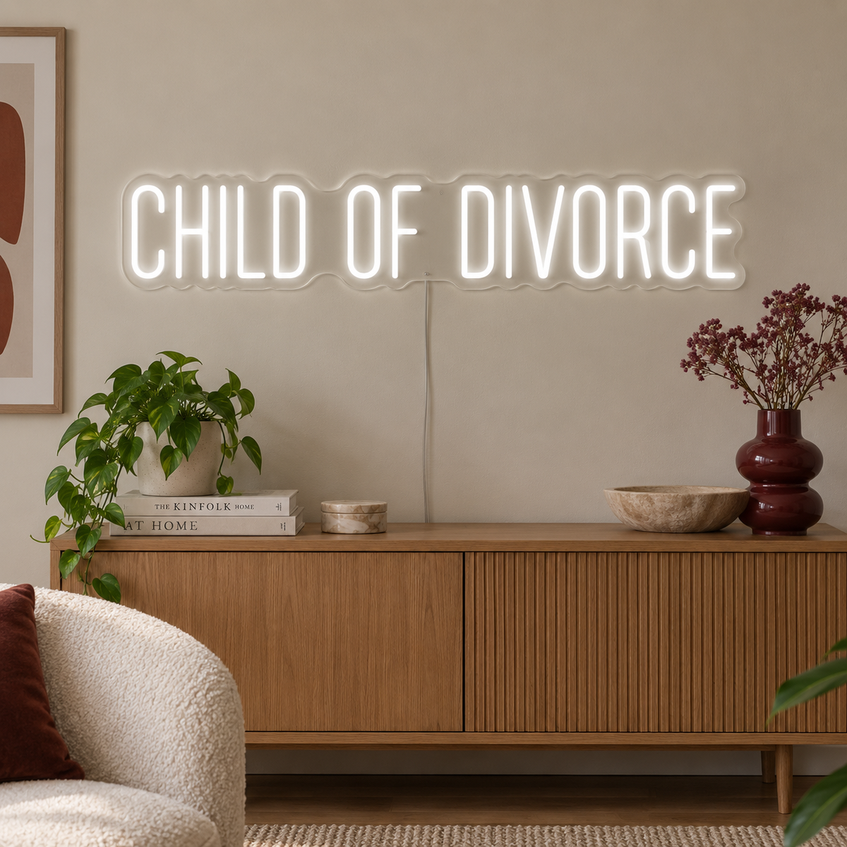 Child Of Divorce Neon Sign, RGB colour-changing option shown in white above a wooden sideboard with plants.