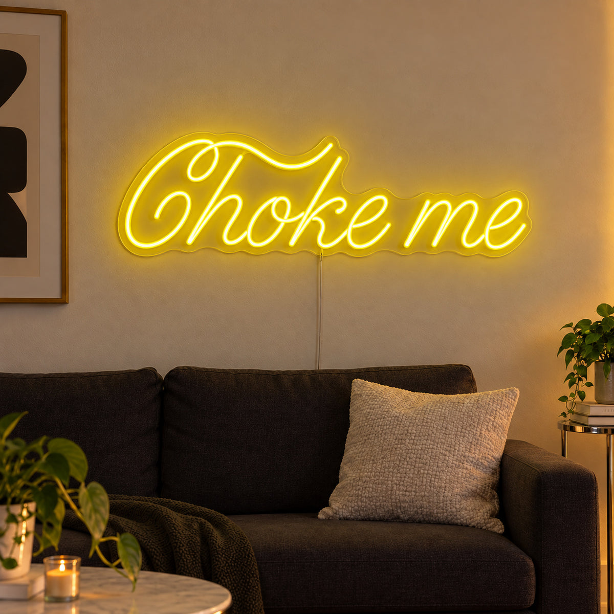 Choke Me Neon Sign with yellow lighting, displayed above a charcoal sofa.
