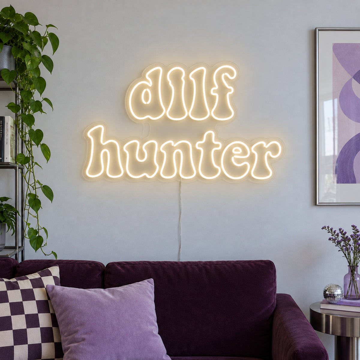 Warm White version of the DILF Hunter Neon Sign, shown above a sofa with purple cushions.