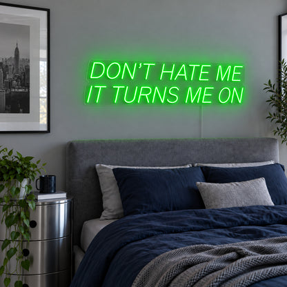 Don't Hate Me It Turns Me On Neon Sign with green lighting, displayed above a bed with dark blue bedding.