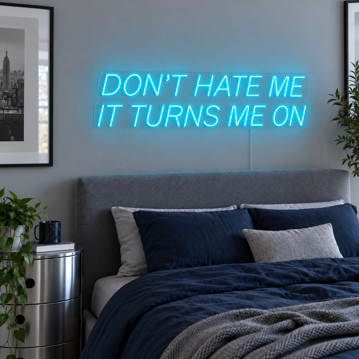 Ice Blue version of the Don't Hate Me It Turns Me On Neon Sign, shown above a bed with dark blue bedding.