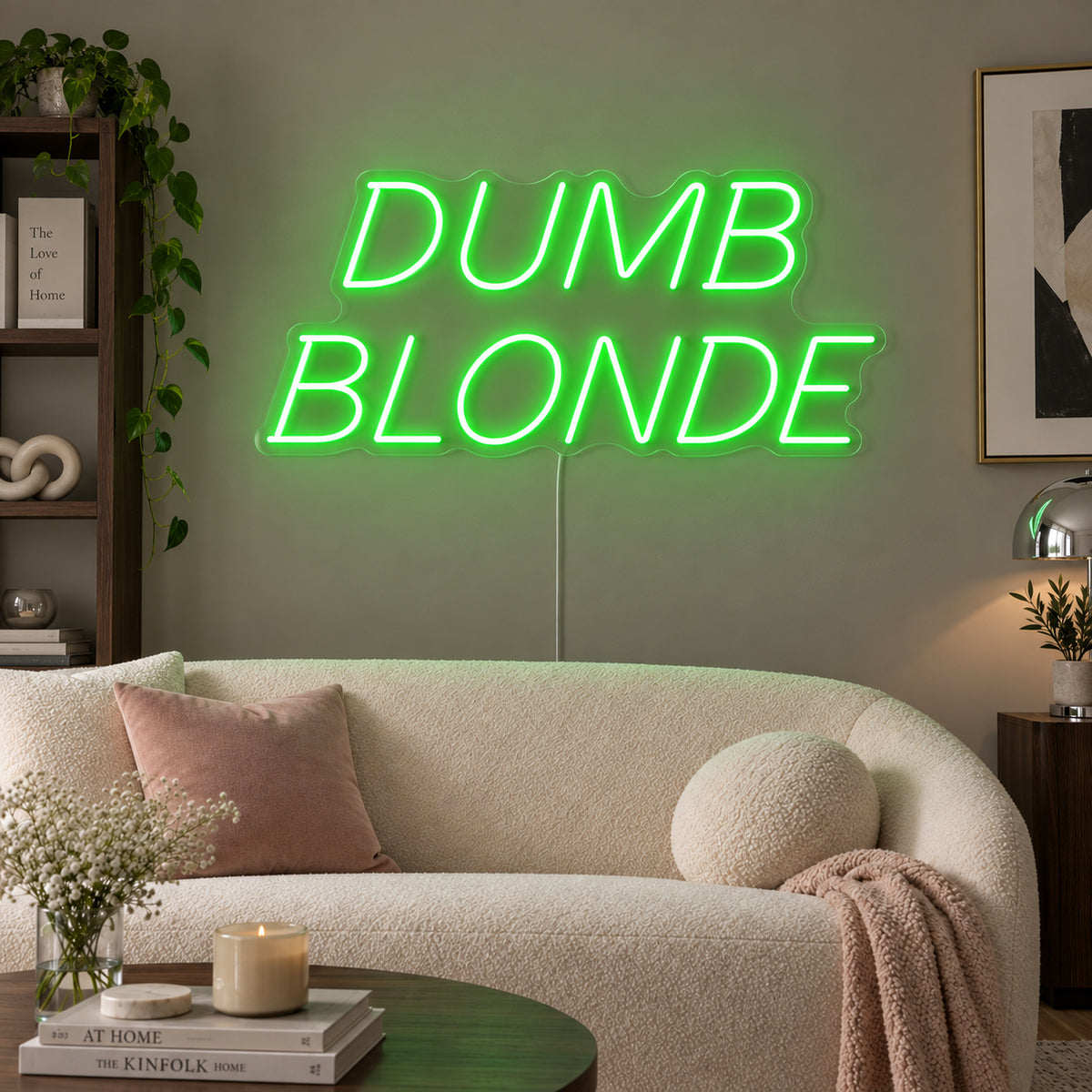 Dumb Blonde Neon Sign with green lighting, displayed in slanted lettering above a cream sofa.