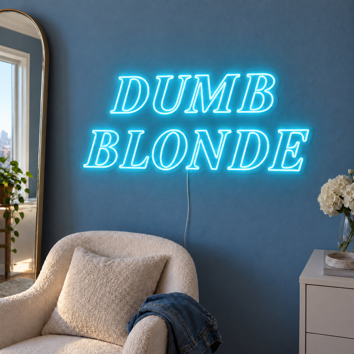 Ice Blue version of the Dumb Blonde Neon Sign, shown in outlined serif lettering above a cream chair.