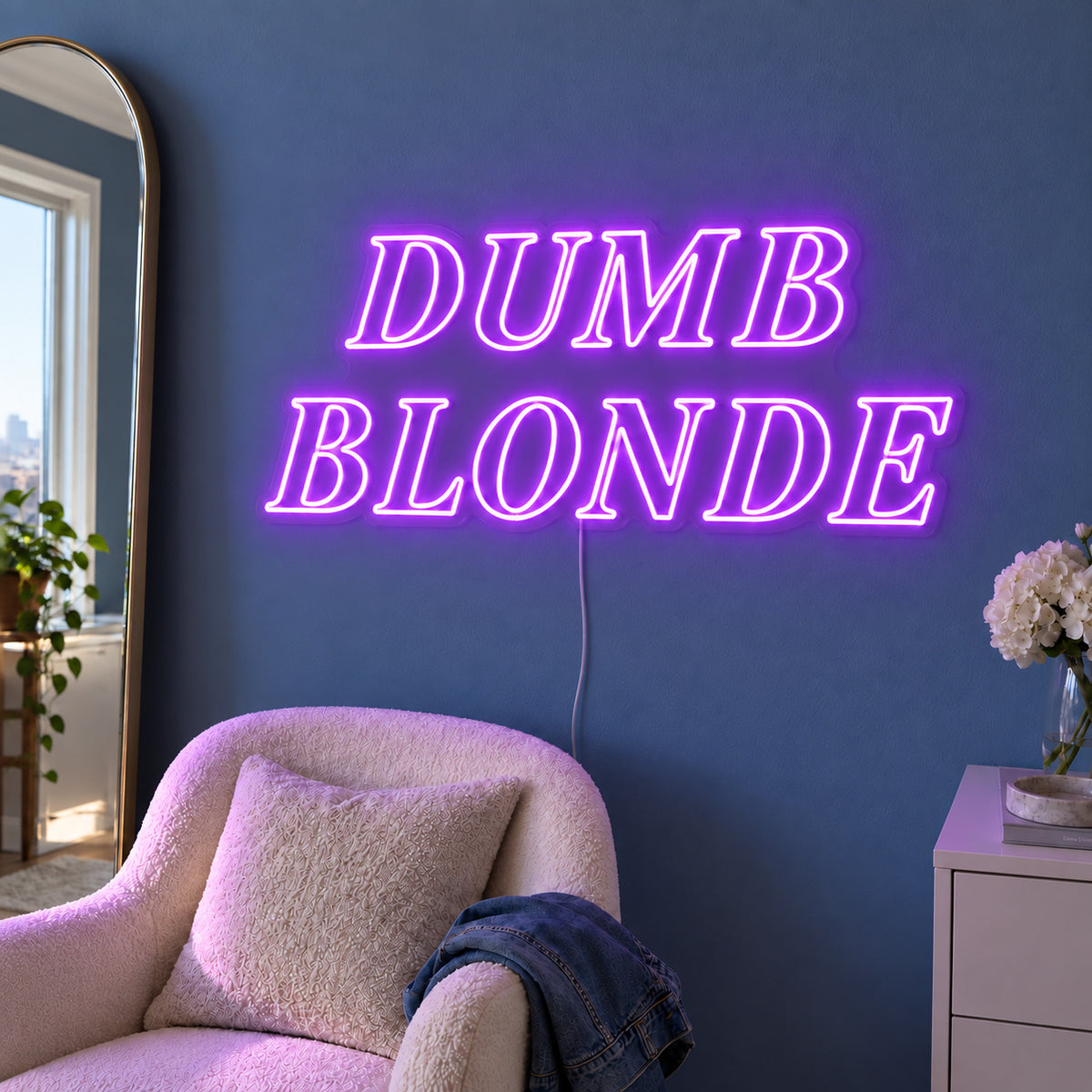 Dumb Blonde Neon Sign with purple lighting, displayed in outlined serif lettering above a cream chair.