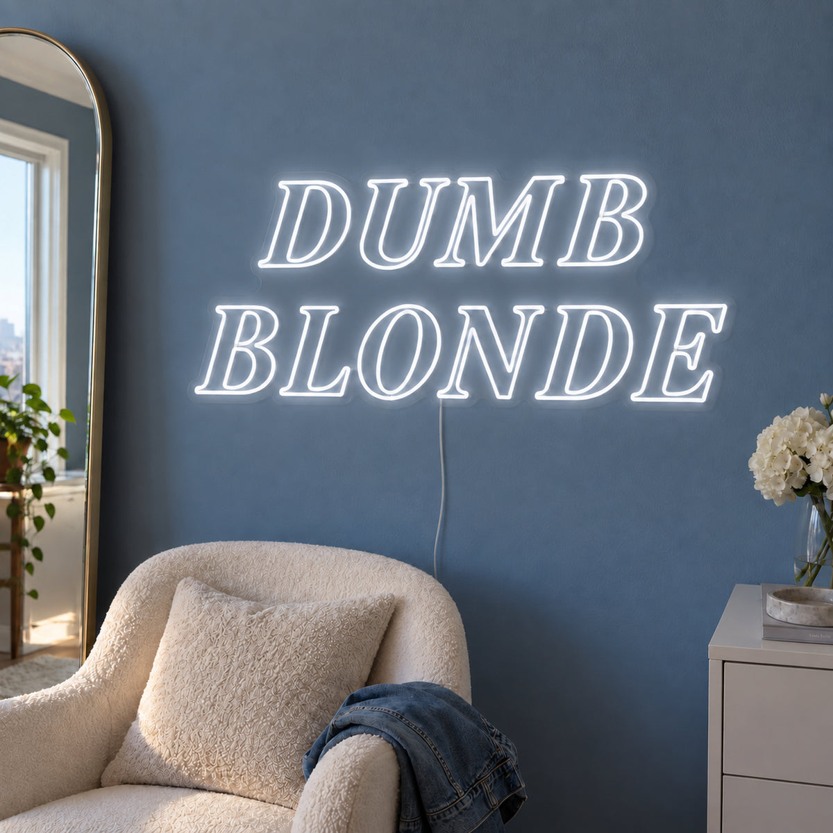 Dumb Blonde Neon Sign in white in outlined serif lettering above a cream chair.