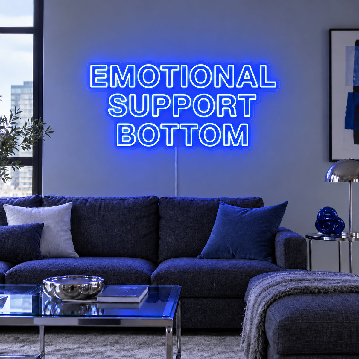 Emotional Support Bottom Neon Sign glowing blue above a charcoal sofa.