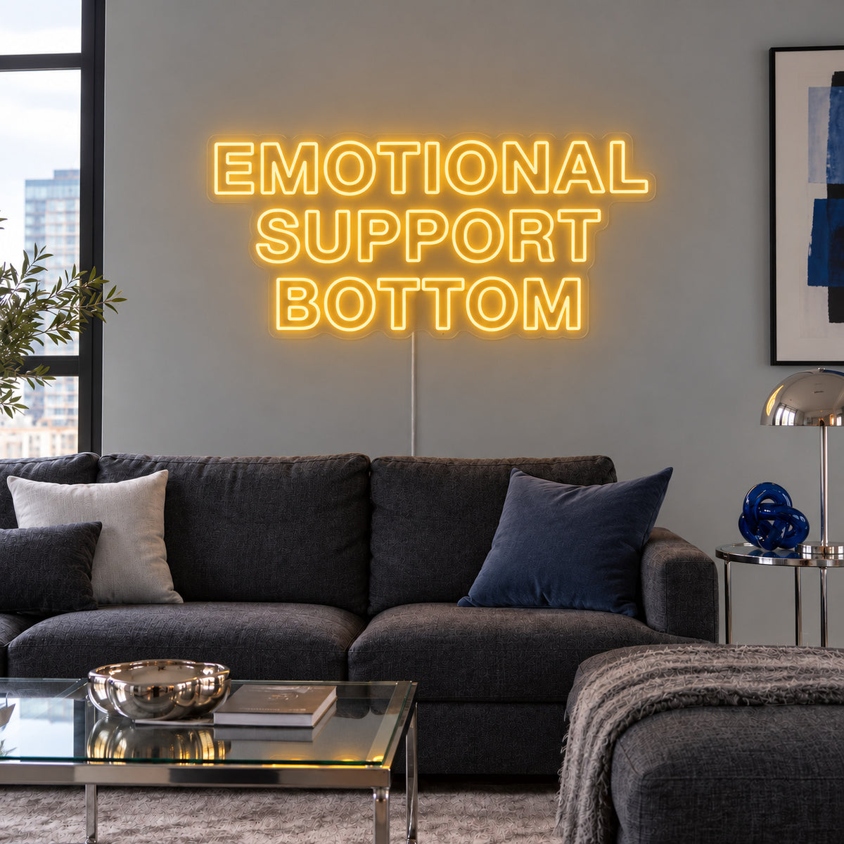 Emotional Support Bottom Neon Sign glowing gold above a charcoal sofa.