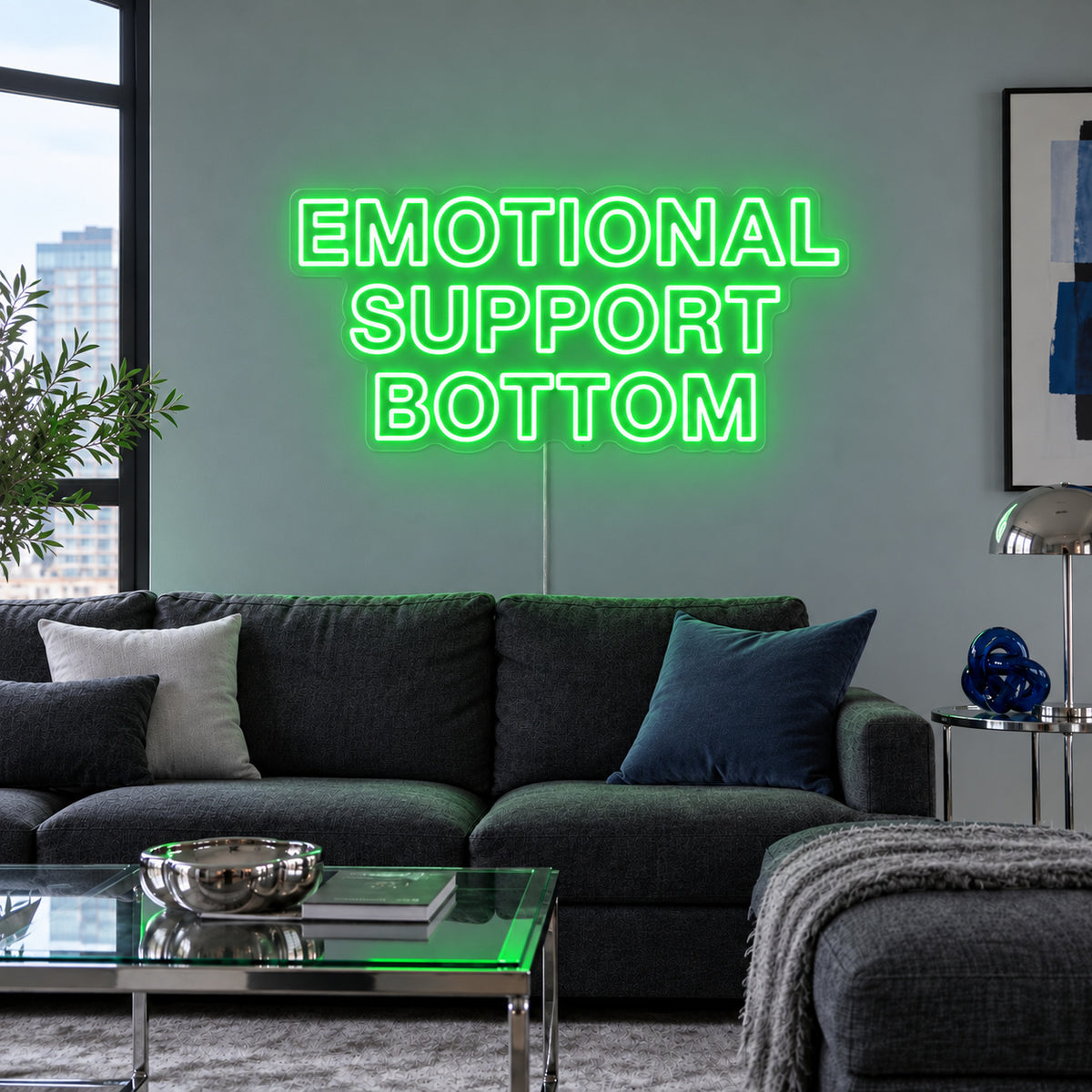 Emotional Support Bottom Neon Sign with green lighting, displayed above a charcoal sofa.