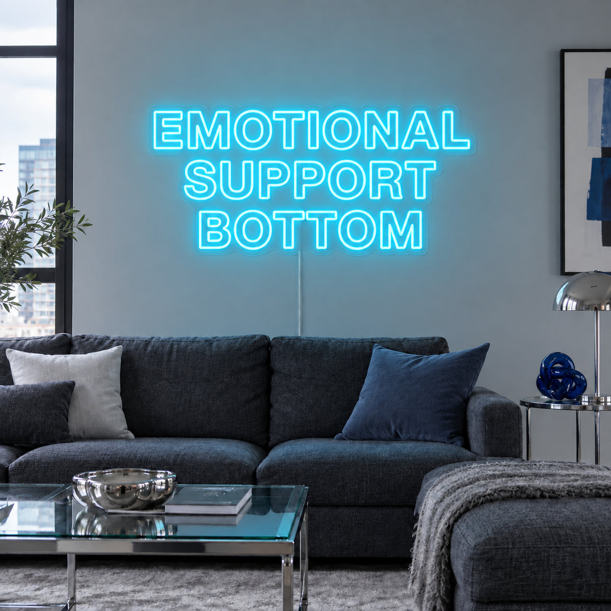 Ice Blue version of the Emotional Support Bottom Neon Sign, shown above a charcoal sofa.