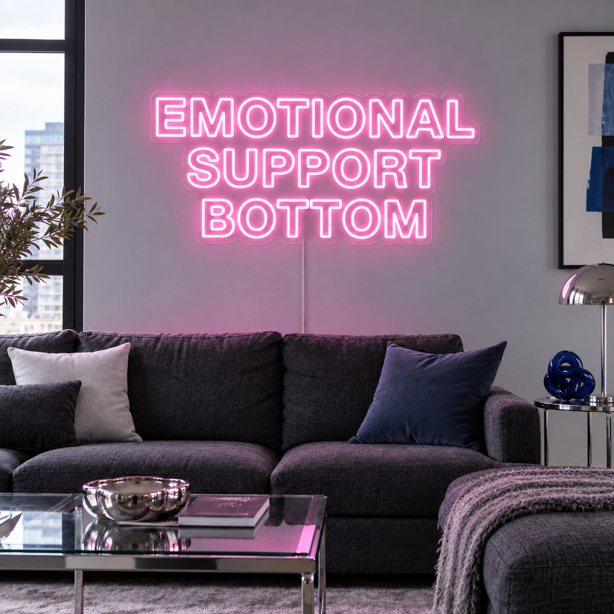 Emotional Support Bottom Neon Sign glowing pink above a charcoal sofa.