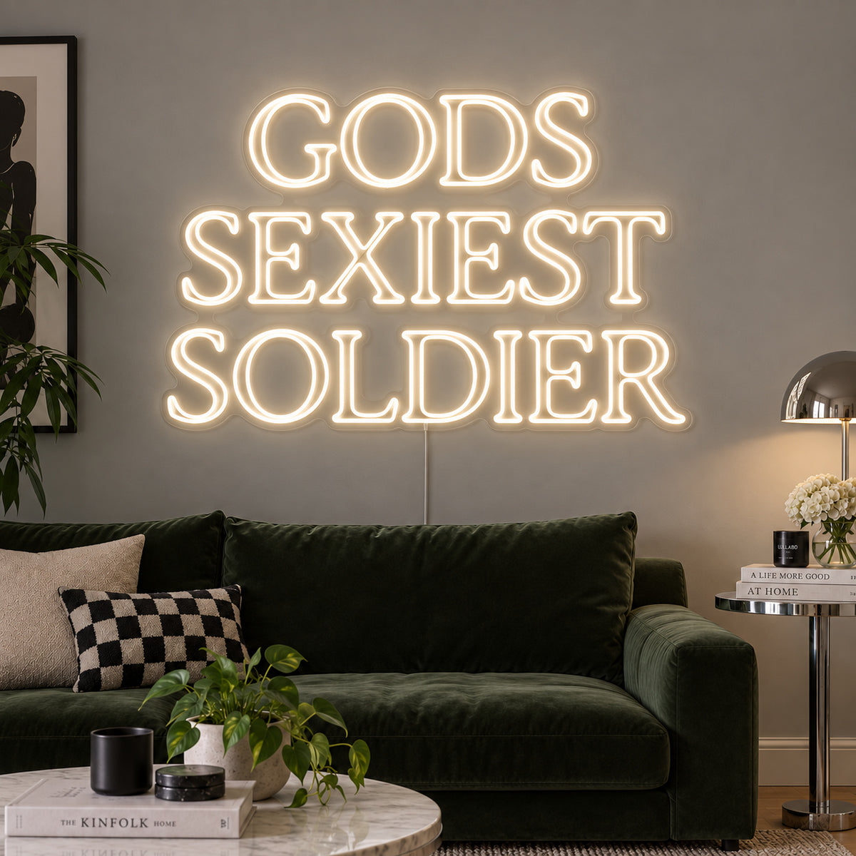 Warm White version of the Gods Sexiest Soldier Neon Sign, shown in outlined serif lettering above a green sofa.