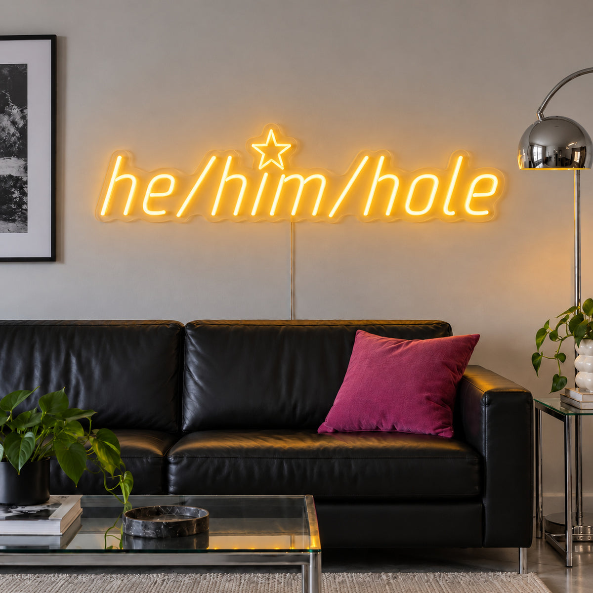 He/Him/Hole Neon Sign glowing gold above a black leather sofa.