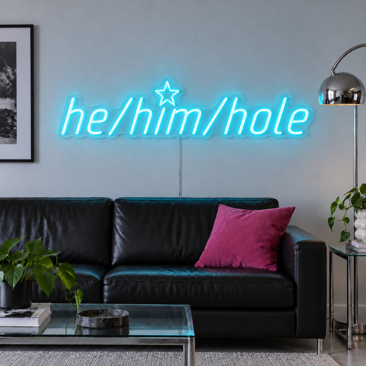 Ice Blue version of the He/Him/Hole Neon Sign, shown above a black leather sofa.