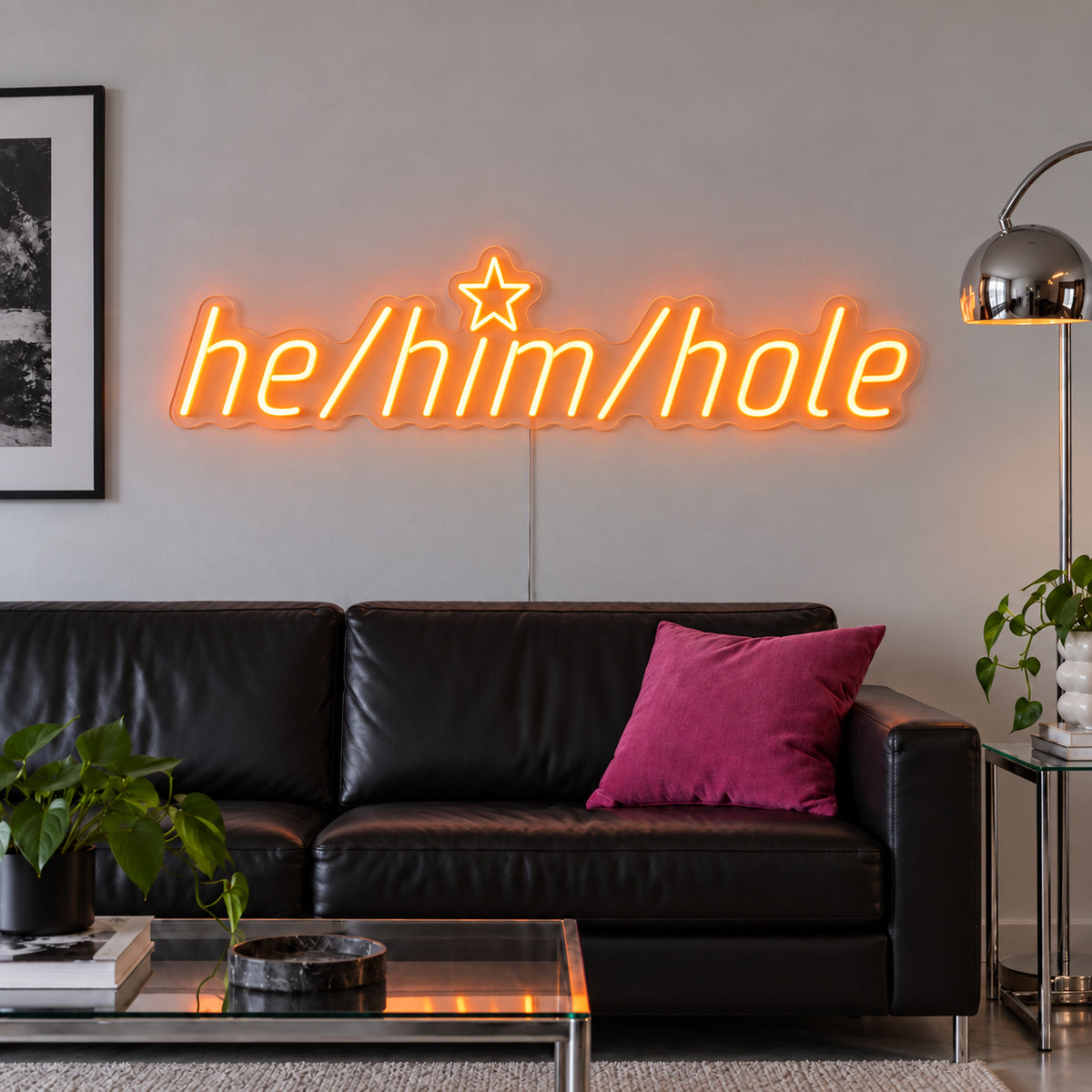 Orange version of the He/Him/Hole Neon Sign, shown above a black leather sofa.