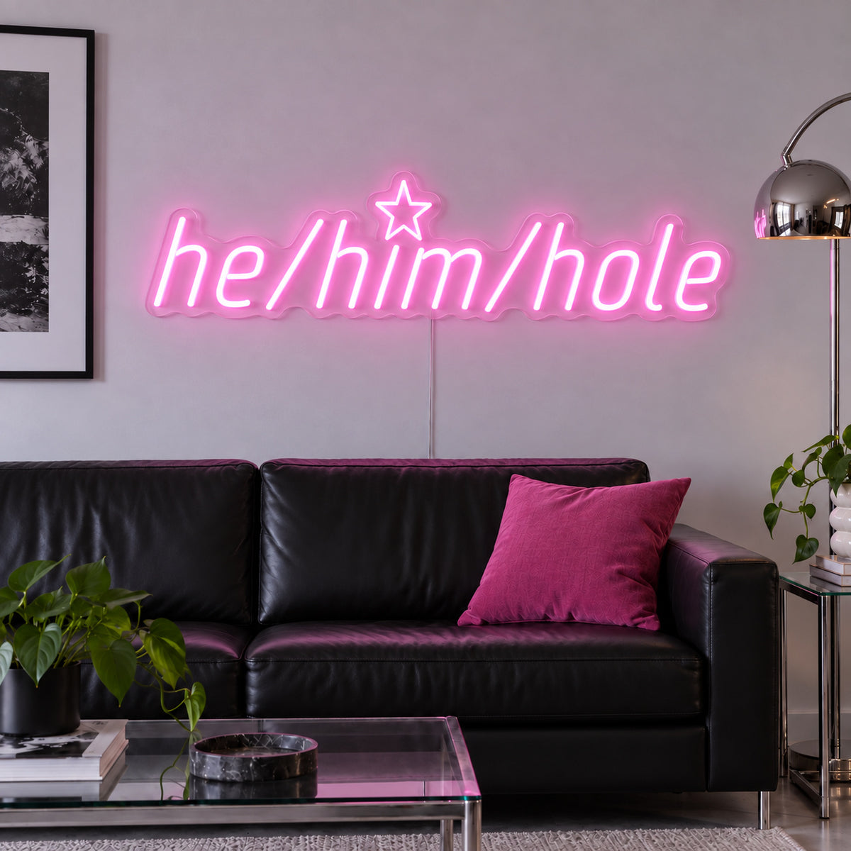 He/Him/Hole Neon Sign glowing pink above a black leather sofa.