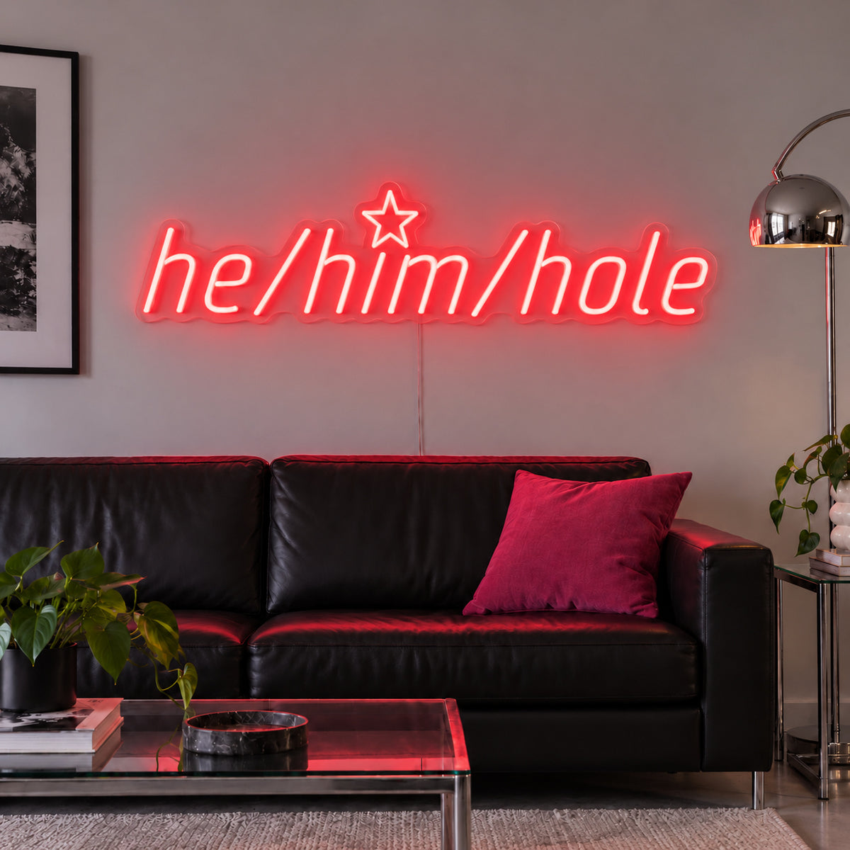 He/Him/Hole Neon Sign with red lighting, displayed above a black leather sofa.
