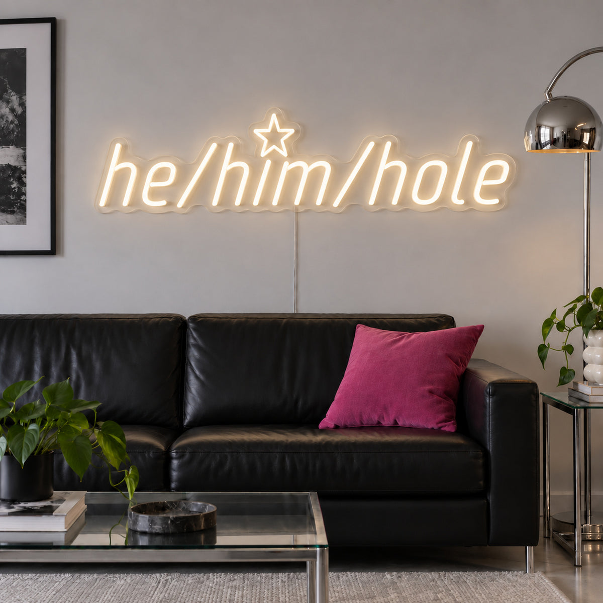 Warm White version of the He/Him/Hole Neon Sign, shown above a black leather sofa.