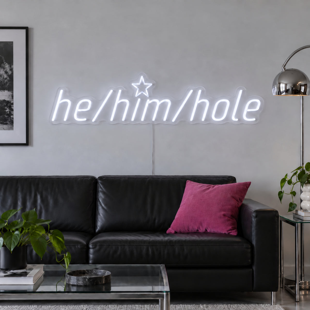 He/Him/Hole Neon Sign in white above a black leather sofa.