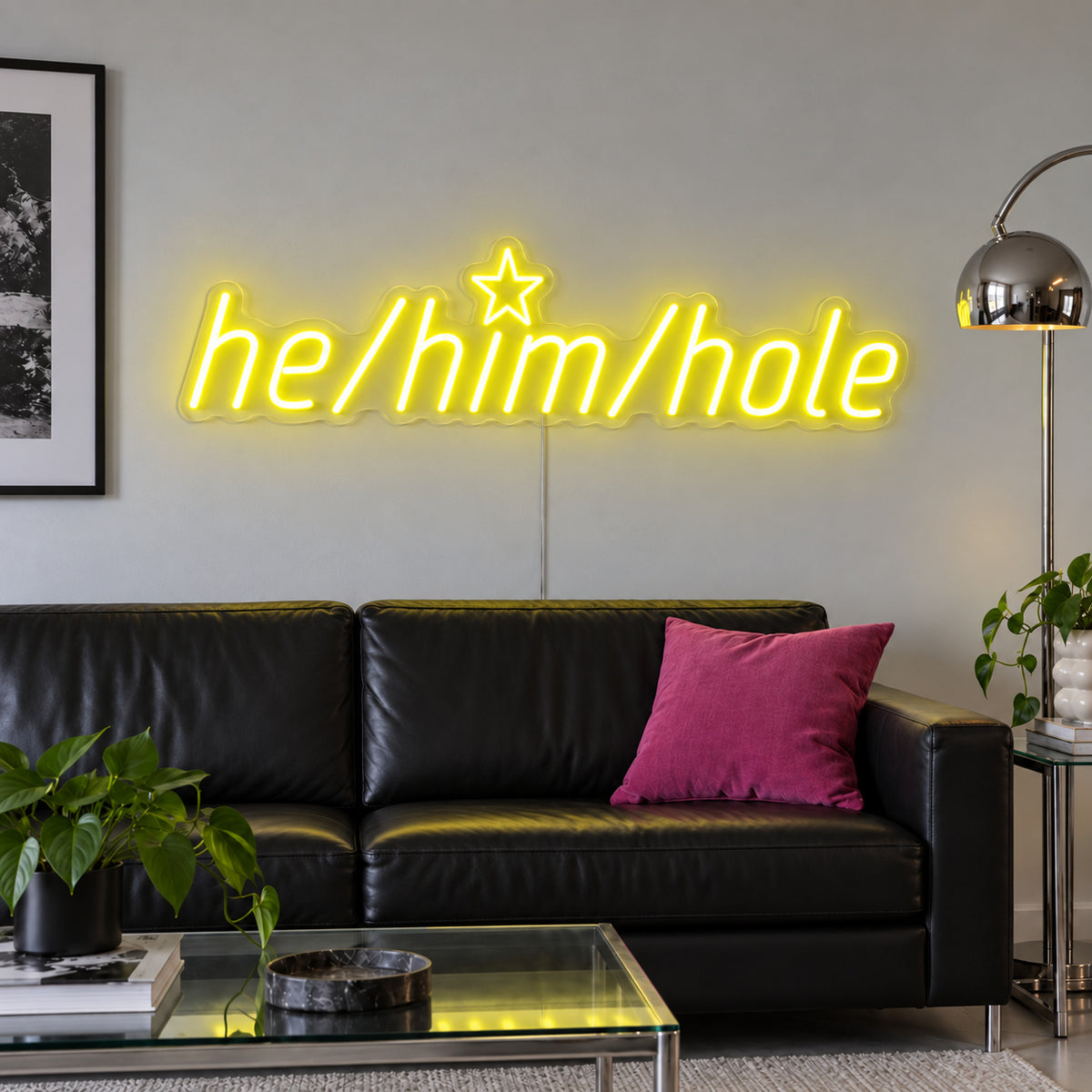 He/Him/Hole Neon Sign with yellow lighting, displayed above a black leather sofa.
