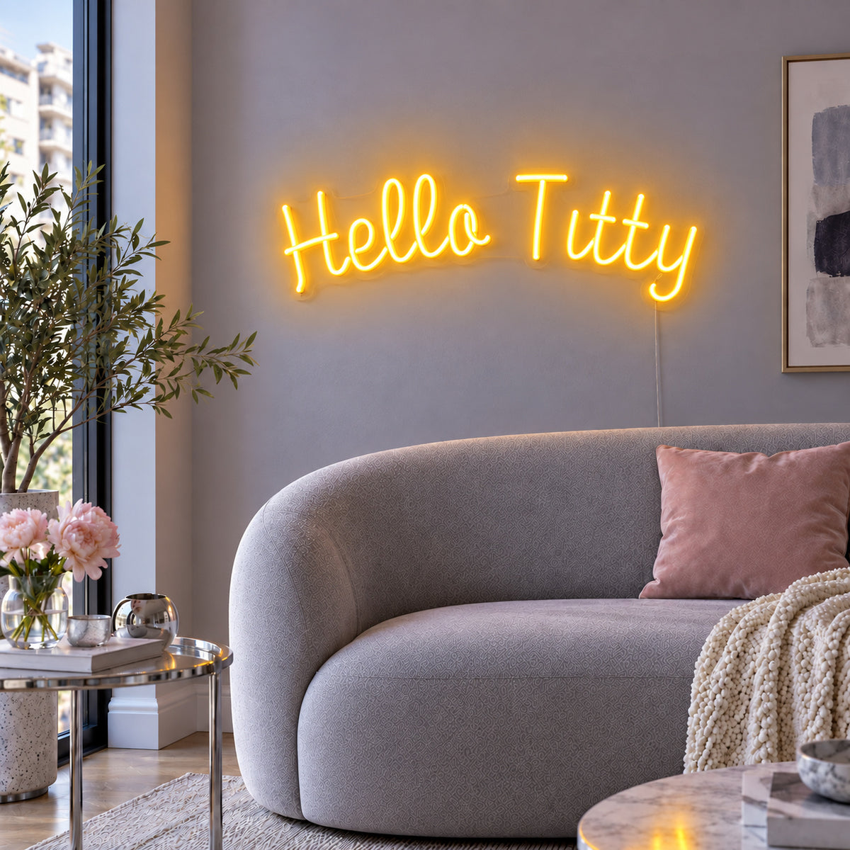 Hello Titty Neon Sign glowing gold above a curved grey sofa.