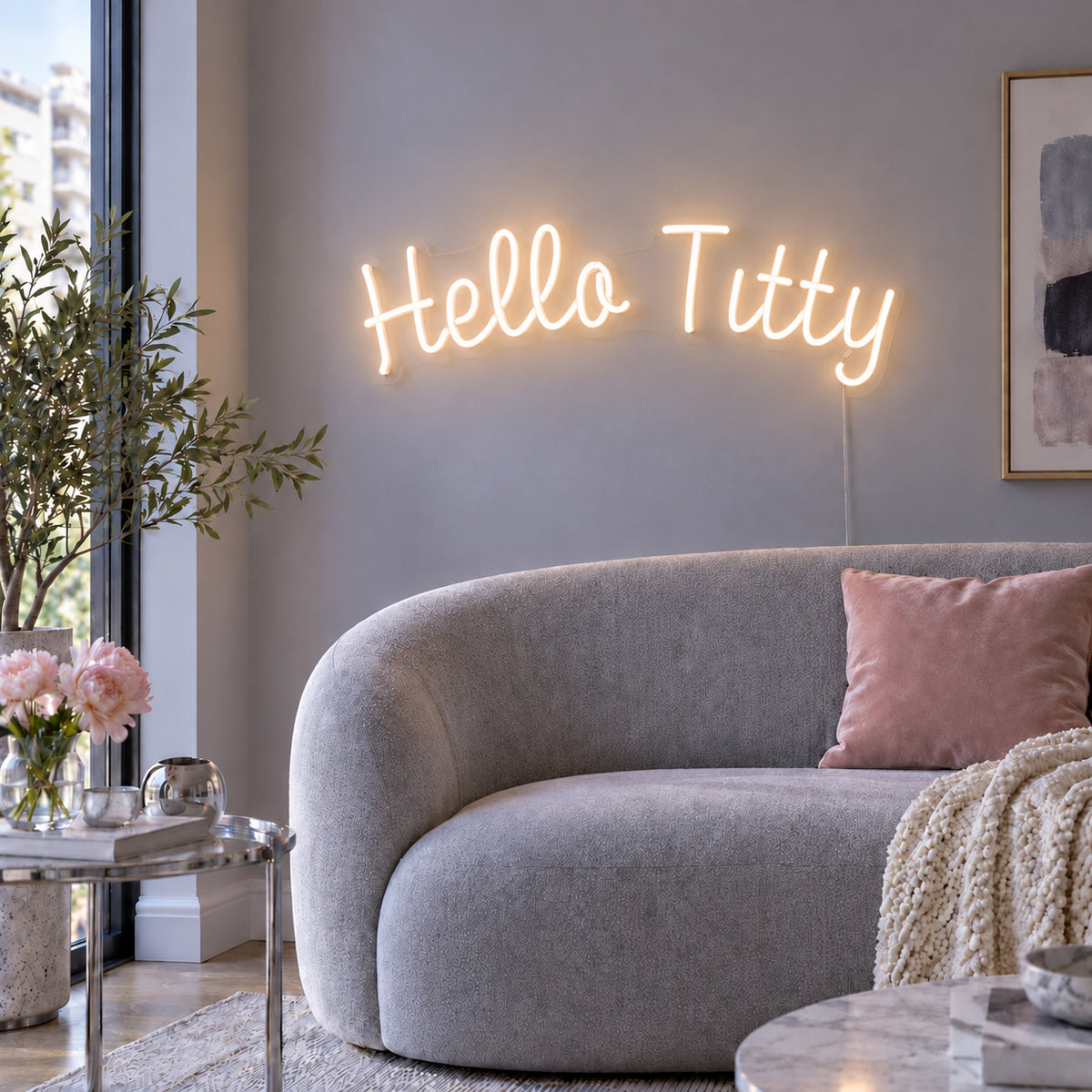 Warm White version of the Hello Titty Neon Sign, shown above a curved grey sofa.