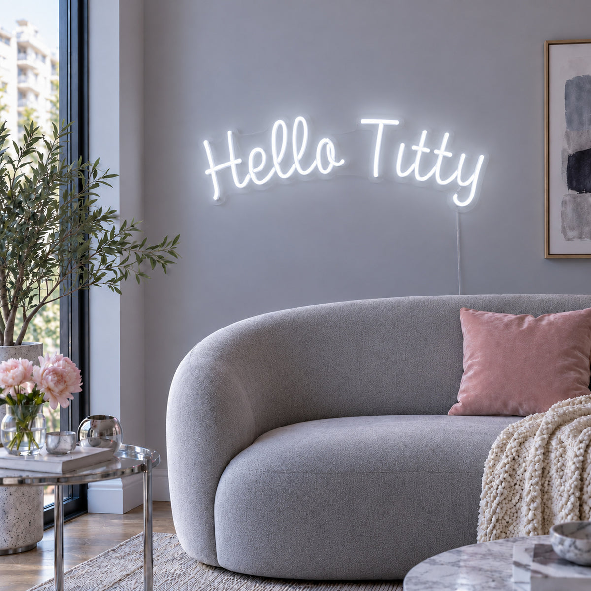 Hello Titty Neon Sign glowing white above a curved grey sofa.