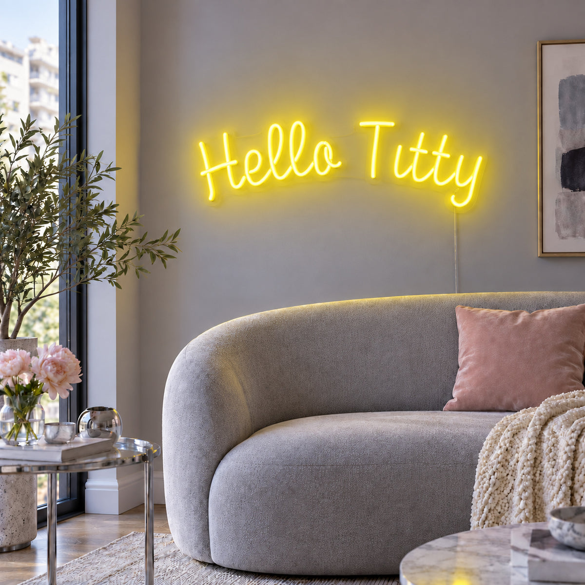 Hello Titty Neon Sign with yellow lighting, displayed above a curved grey sofa.