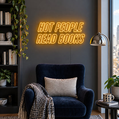 Hot People Read Books Neon Sign glowing gold above a blue reading chair.