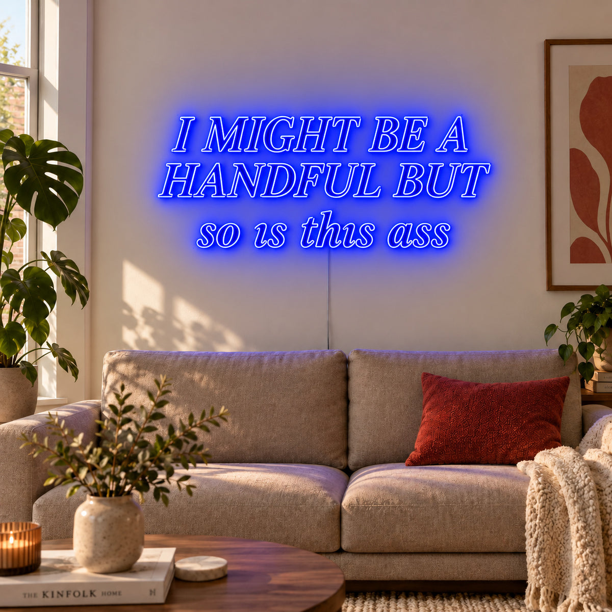 I Might Be A Handful But So Is This Ass Neon Sign glowing blue in compact lettering above a cream sofa.