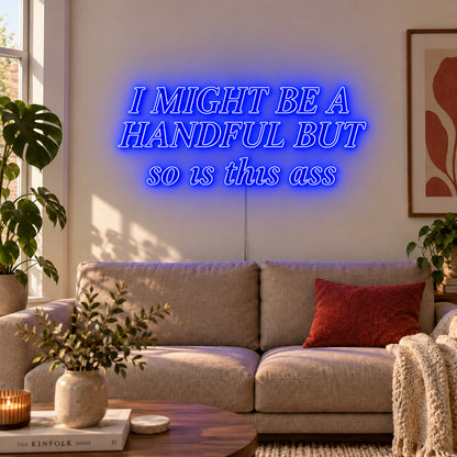 I Might Be A Handful But So Is This Ass Neon Sign glowing blue in compact lettering above a cream sofa.