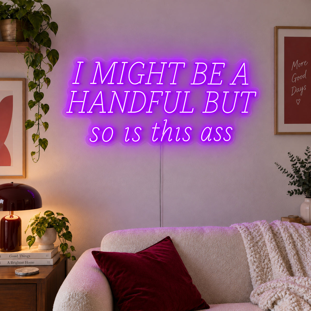 I Might Be A Handful But So Is This Ass Neon Sign with purple lighting, displayed in wide lettering above a cream sofa.