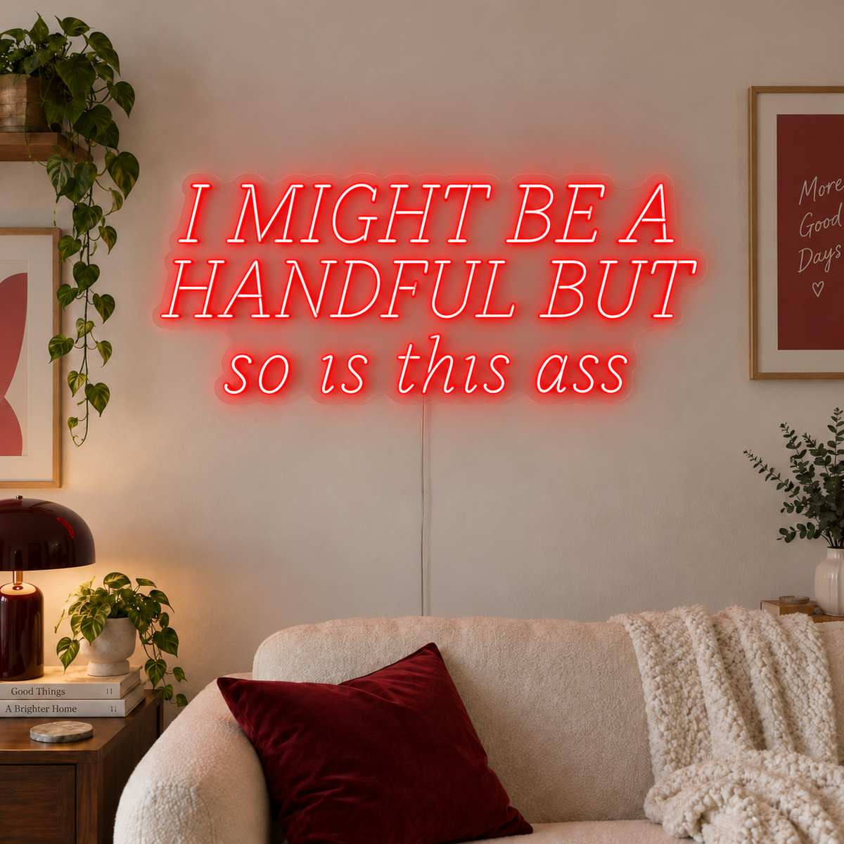 I Might Be A Handful But So Is This Ass Neon Sign in red in wide lettering above a cream sofa.