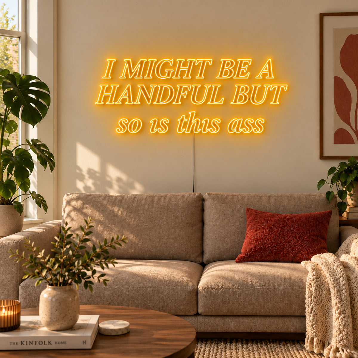 I Might Be A Handful But So Is This Ass Neon Sign glowing gold in compact lettering above a cream sofa.