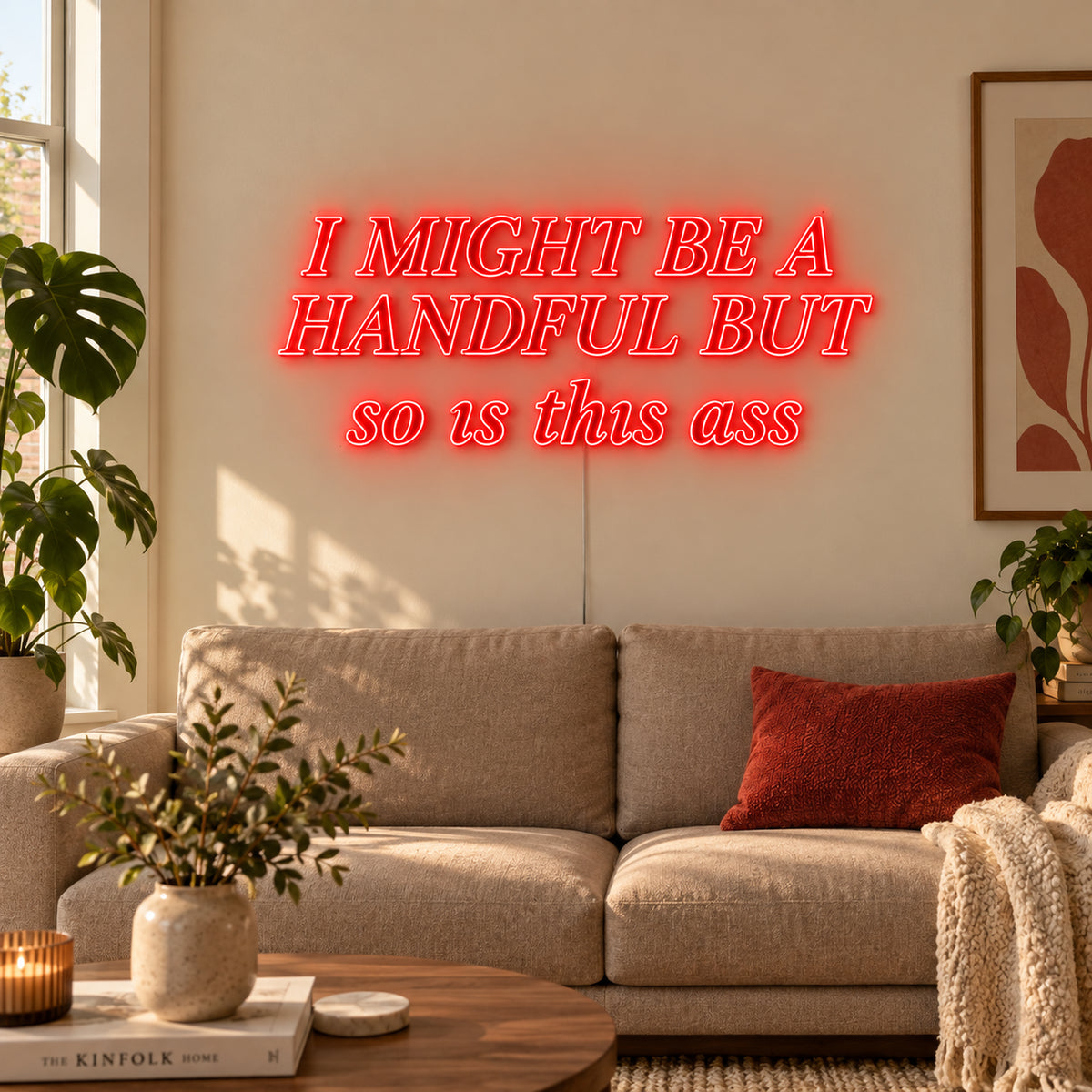I Might Be A Handful But So Is This Ass Neon Sign in red in compact lettering above a cream sofa.