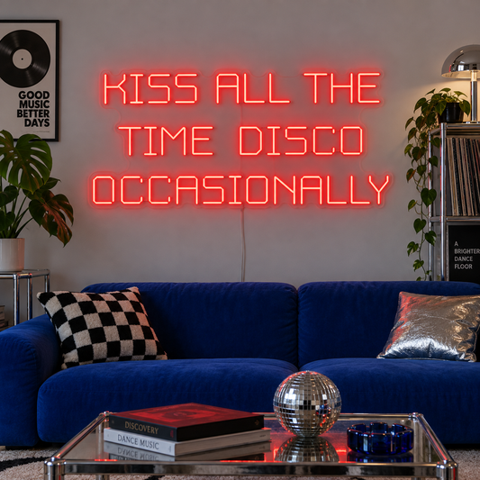 Kiss All The Time Disco Occasionally Neon Sign in red above a blue sofa near a disco ball.