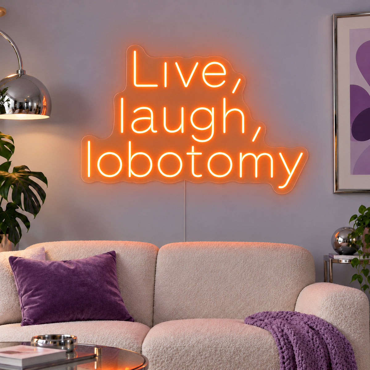 Orange version of the Live, Laugh, Lobotomy Neon Sign, shown above a cream sofa with purple cushions.
