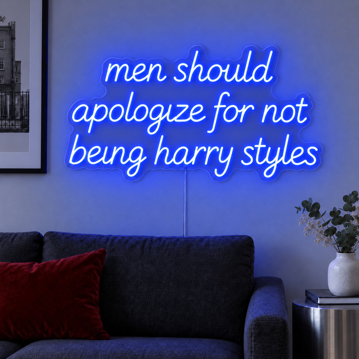 Men Should Apologize For Not Being Harry Styles Neon Sign glowing blue above a dark sofa.