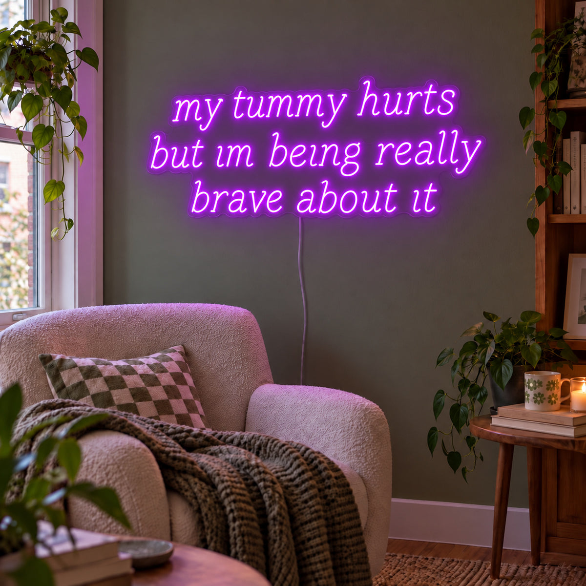 My Tummy Hurts But Im Being Really Brave About It Neon Sign with purple lighting, displayed above a reading chair against a green wall.