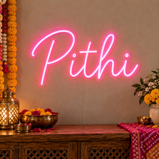 Pithi Neon Sign on clear cut-to-shape acrylic, illuminated on a wall in a styled celebration setting